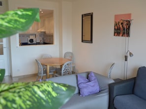 Un salon moderne avec un canapé gris, une table à manger en bois et une cuisine en arrière-plan.