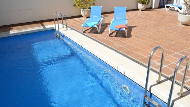 Une piscine à l’eau bleue, deux chaises longues et des plantes en pot.