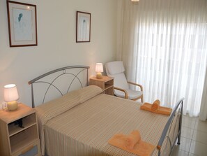 Une chambre d’hôtel avec un lit, une chaise, une table de chevet avec une lampe et deux tableaux encadrés au mur.