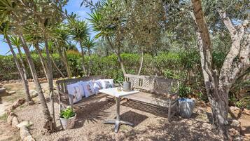 An outdoor seating area with a table and benches, surrounded by trees and plants.