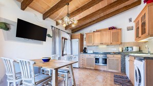 Une cuisine avec des meubles en bois, un four encastré, un lave-linge et un coin repas comprenant une table et des chaises.