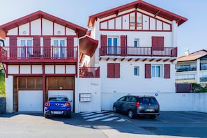 Un bâtiment à deux étages aux couleurs rouge et blanche, doté de balcons, d’un garage et d’un espace de stationnement.