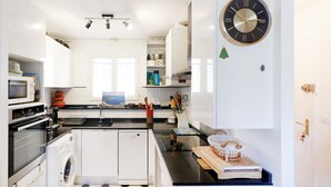 Una cocina moderna con armarios blancos, horno empotrado, lavavajillas y un gran reloj de pared.