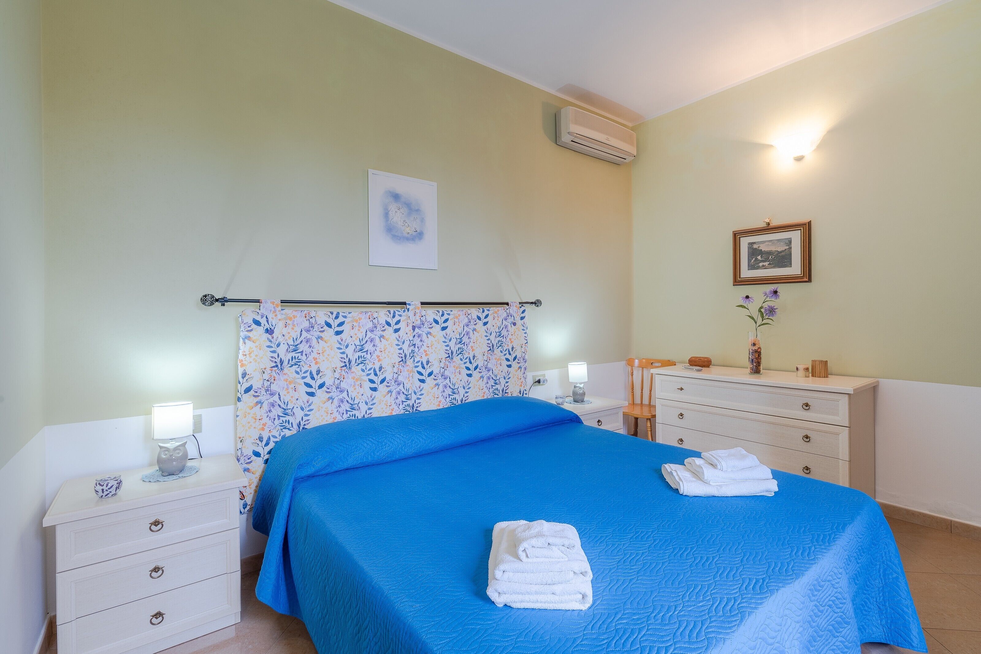 Ein Schlafzimmer mit einem Bett, Nachttischen, einem Schminktisch, einer Kommode, einer Klimaanlage und einer Wandleuchte.