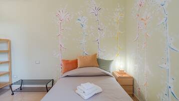 A neatly made bed with pillows, a bedside table with a lamp, and a wall with floral wall art.