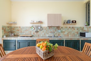 A kitchen with a tiled backsplash, wooden cabinets, a dining table with chairs, and a basket of fruit on the table. - Holiday Home 'Ciumara West' with Private Terrace, Wi-Fi and Air Conditioning (Avola)