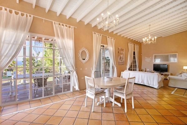 A room with a dining table, chairs, a TV, and a bed.
