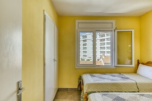 Une chambre avec deux lits, une fenêtre donnant sur des immeubles, une porte et un miroir.