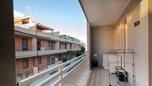 Un balcón con un tendedero de metal, un bote de basura y vistas de un edificio de varios pisos con balcones.