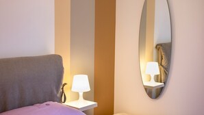 Una habitación de hotel con cama, lámpara de noche, espejo y mesita de noche.