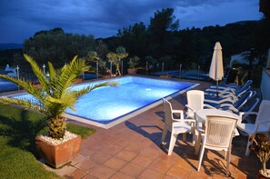 A rectangular swimming pool with a tiled deck, surrounded by white lounge chairs and a table, with potted plants and a palm tree nearby. - Villa 'Estrella' with Mountain View, Wi-Fi and Air Conditioning (La Torre Vella)