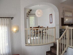 Un espace repas avec vue sur la cuisine, un escalier et un lustre.