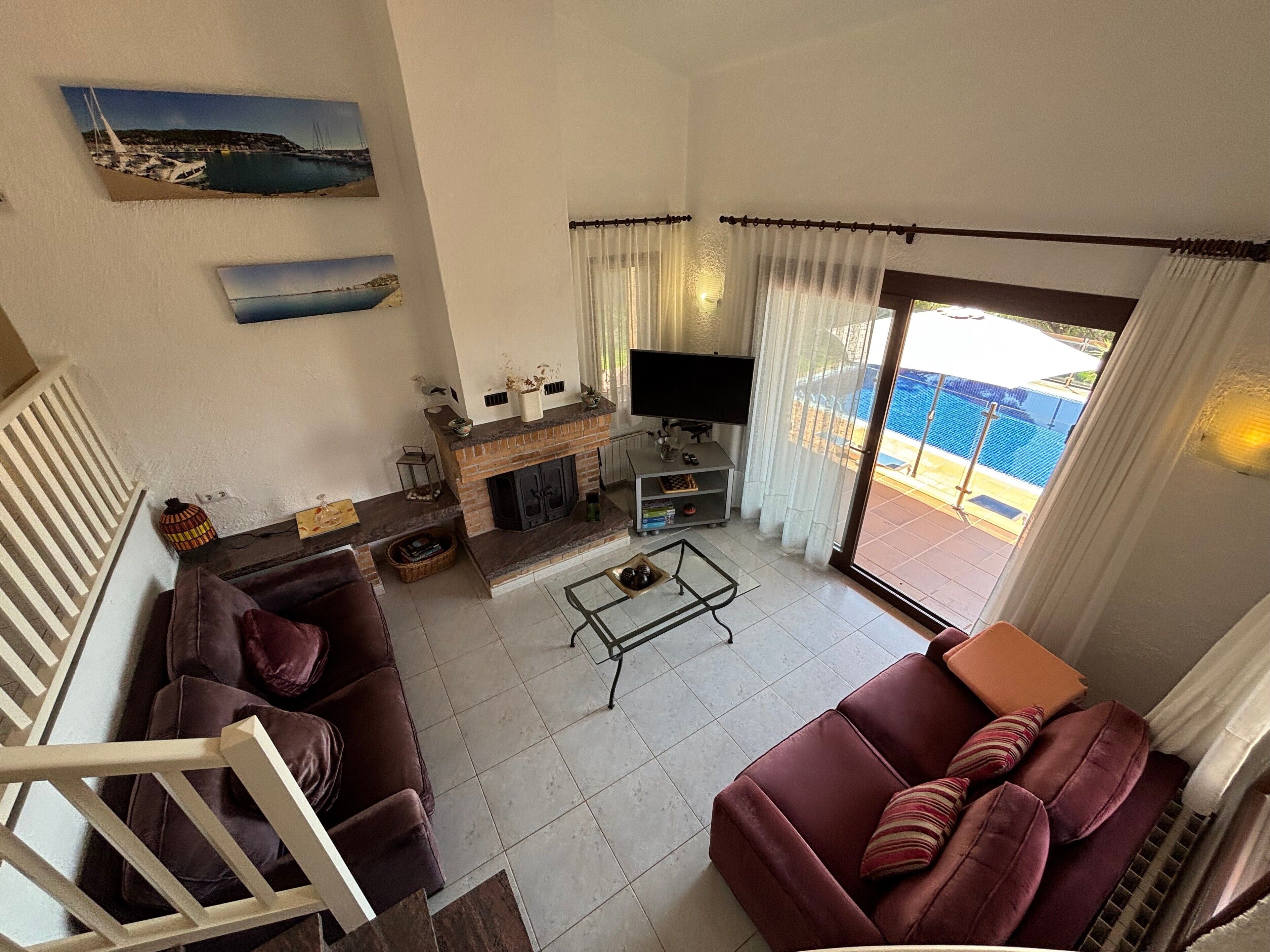 Una sala de estar con chimenea, televisor, sofá y vista a una piscina.