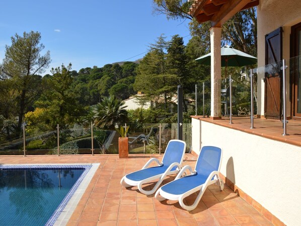 Un espace piscine aménagé avec des chaises longues, une pergola et une vue sur une colline boisée.