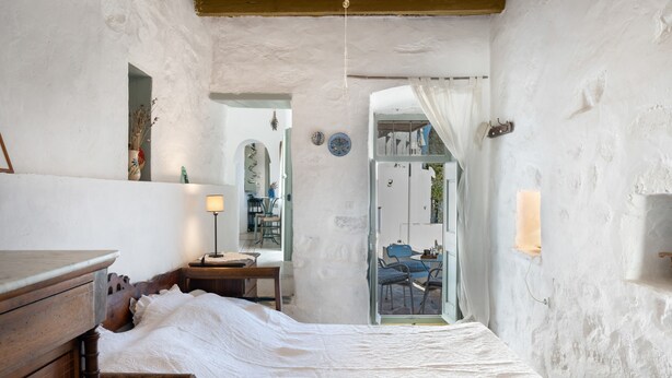 Une chambre à coucher avec un lit en bois, une table de chevet, une lampe et une vue sur l’extérieur par une porte.
