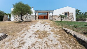 A white building with a stone facade, a covered entrance, and a tree in the foreground. - Villa 'Pedduzza' with Sea View, Private Terrace and Wi-Fi (Orosei NU)