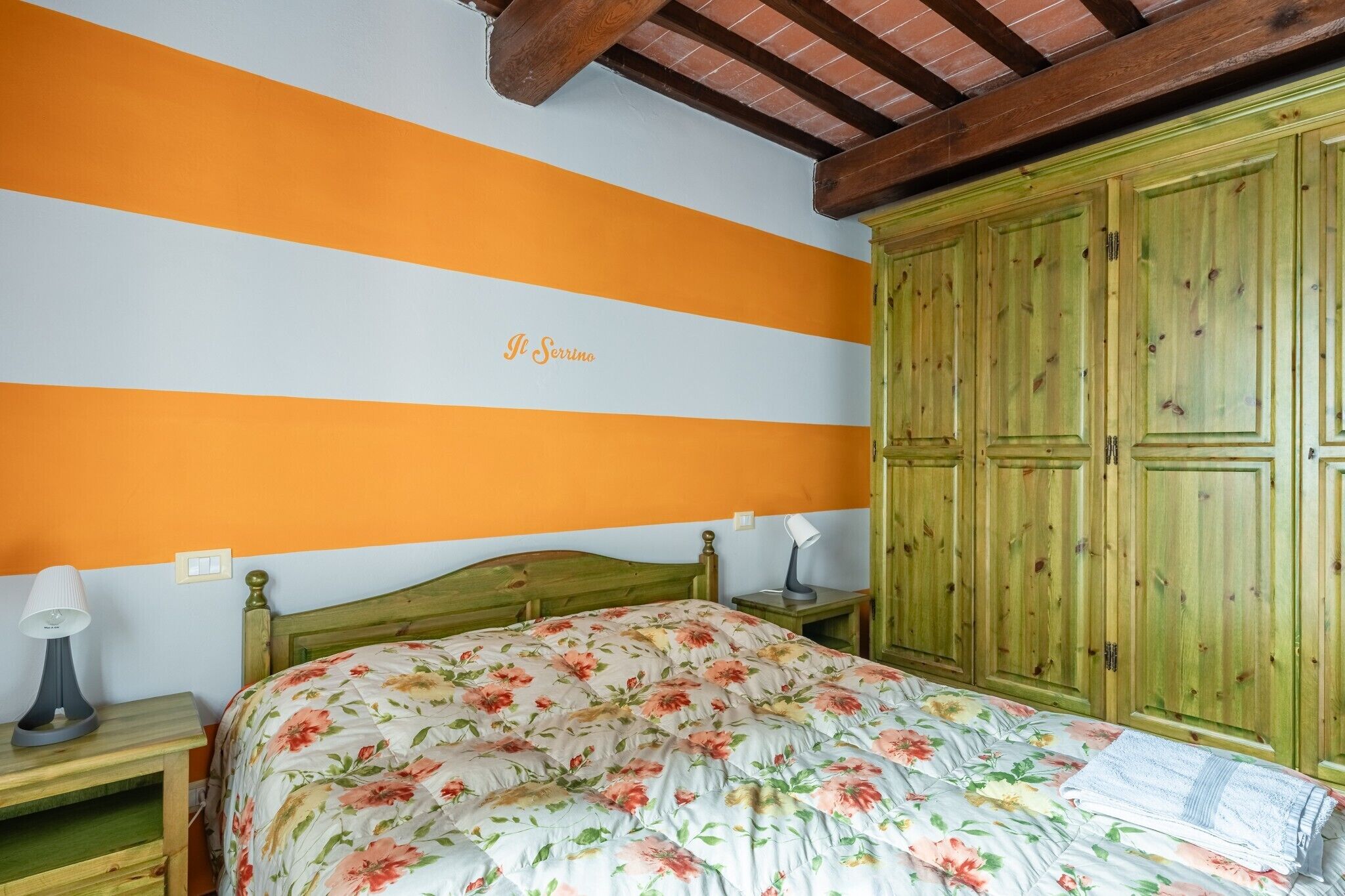 Quarto com cama, guarda-roupa de madeira e parede com listras laranja e branca.