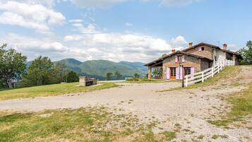 A rustic stone building with a white fence, a gravel path, and a view of mountains.