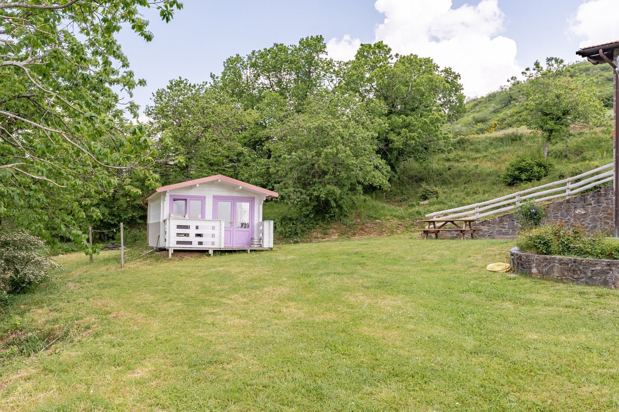 Un petit bâtiment d’un seul étage, avec une porte et des fenêtres violettes, entouré d’une pelouse et d’arbres.