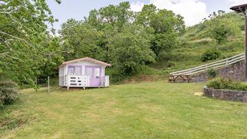 Un petit bâtiment d’un seul étage, avec une porte et des fenêtres violettes, entouré d’une pelouse et d’arbres.