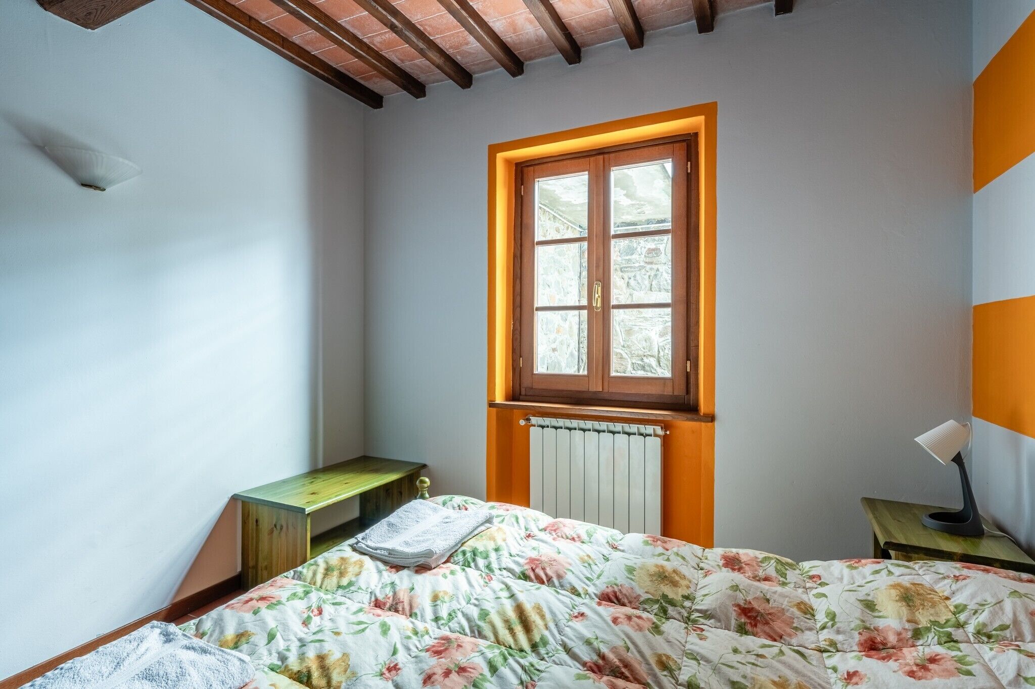 Quarto com cama, janela, radiador, mesa de cabeceira e abajur.