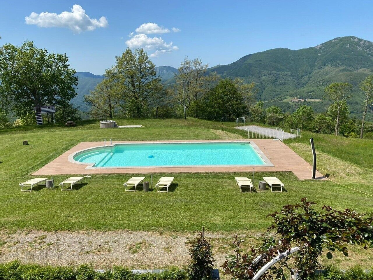 A rectangular swimming pool with a wooden deck, surrounded by a grassy area with white lounge chairs.