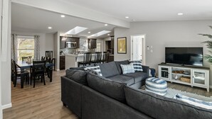 A modern living room with a grey sectional sofa, a dining area with a wooden table and chairs, and a kitchen in the background. - Dock is waiting!  Fishing, paddleboards, kayaking!!
Come relax by the Lake! (Copake)