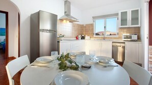 Una cocina moderna con gabinetes blancos, electrodomésticos de acero inoxidable y una zona de comedor para cuatro.