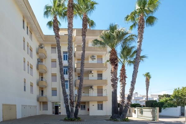 A multi-story building with balconies, palm trees, and a gated entrance.