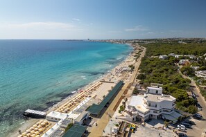 An aerial view of a coastal area with a beach, buildings, and a road.