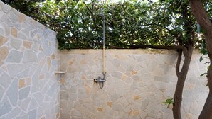 A stone-walled outdoor shower area with a metal showerhead, surrounded by greenery. - Apartment 'Casa Vacanze Colopi' with Private Garden (Gallipoli)