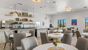 A modern dining area with round tables and chairs, a kitchen counter with a coffee machine, and large windows offering a view of the desert landscape. - Taawaki Inn - Cottonwood. (Clarkdale)