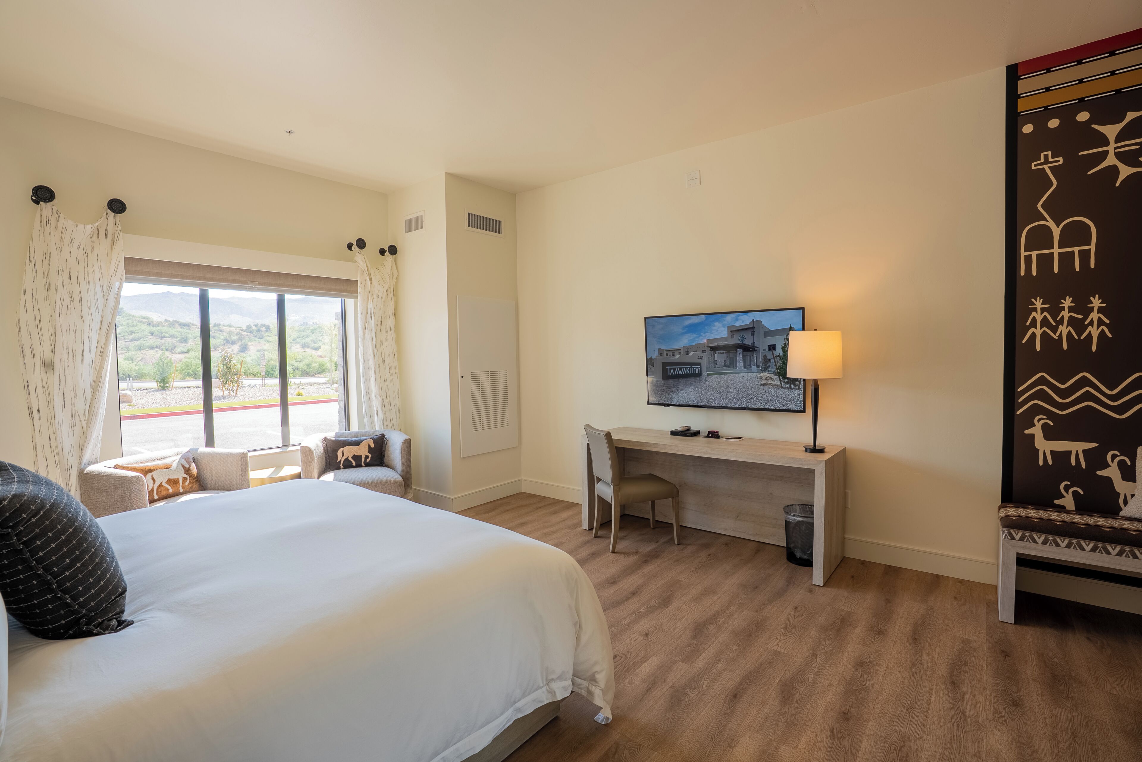 Habitación de hotel con cama, escritorio, silla, televisión y vistas al exterior.