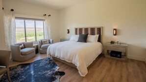 A bedroom with a large bed, two bedside tables, a chair, a rug, and a view of the outdoors. - Taawaki Inn - Cottonwood. (Clarkdale)
