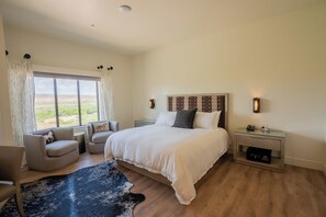 A bedroom with a large bed, two bedside tables, a chair, a rug, and a view of the outdoors. - Taawaki Inn - Cottonwood. (Clarkdale)