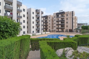 Un immeuble d’appartements moderne doté d’une piscine, entouré de haies bien entretenues et d’un chemin en pierre.