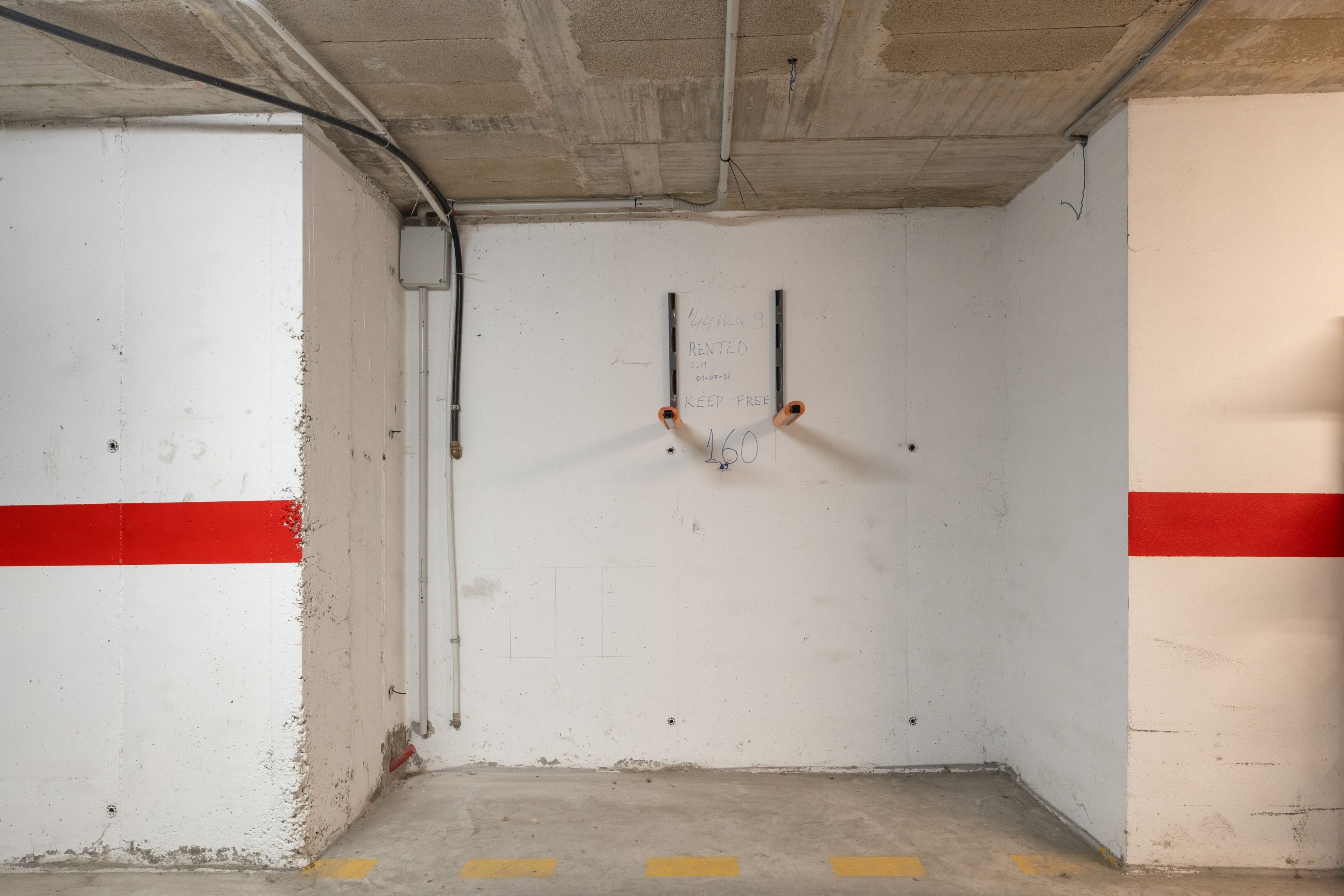 Een parkeergarage met betonnen muren, een rode streep en een gele lijn op de vloer.