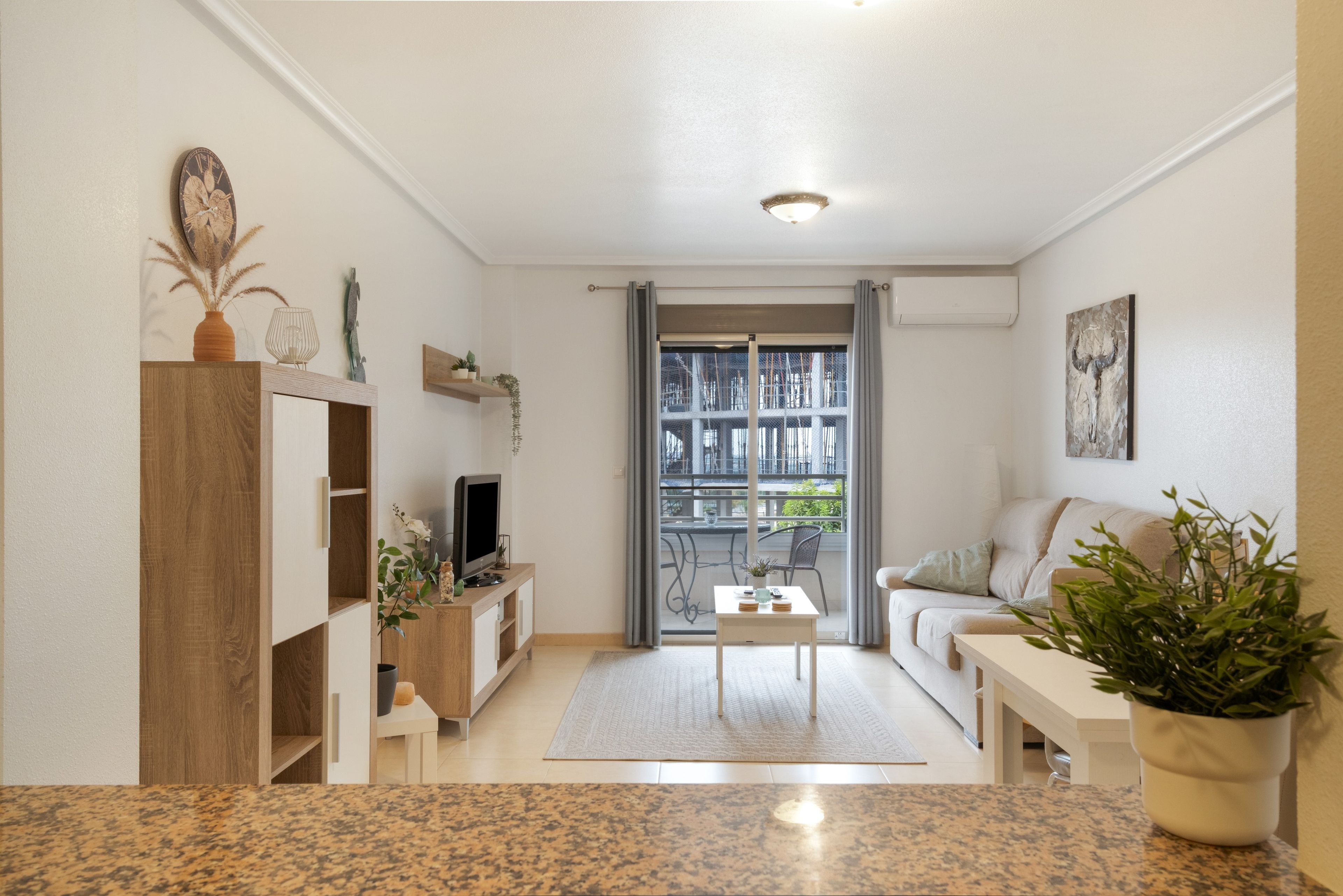 Un soggiorno moderno con televisione, tavolino da caffè e divano. Una finestra offre vista sui palazzi circostanti.