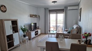 A modern living room with a TV, seating, a dining area, and a balcony with a view. - Apartment 'Carpediem in Spanje' with Lake View, Shared Pool and Wi-Fi (San Miguel de Salinas)