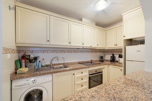 A kitchen with white cabinets, a granite countertop, a washing machine, a dishwasher, and a stove.