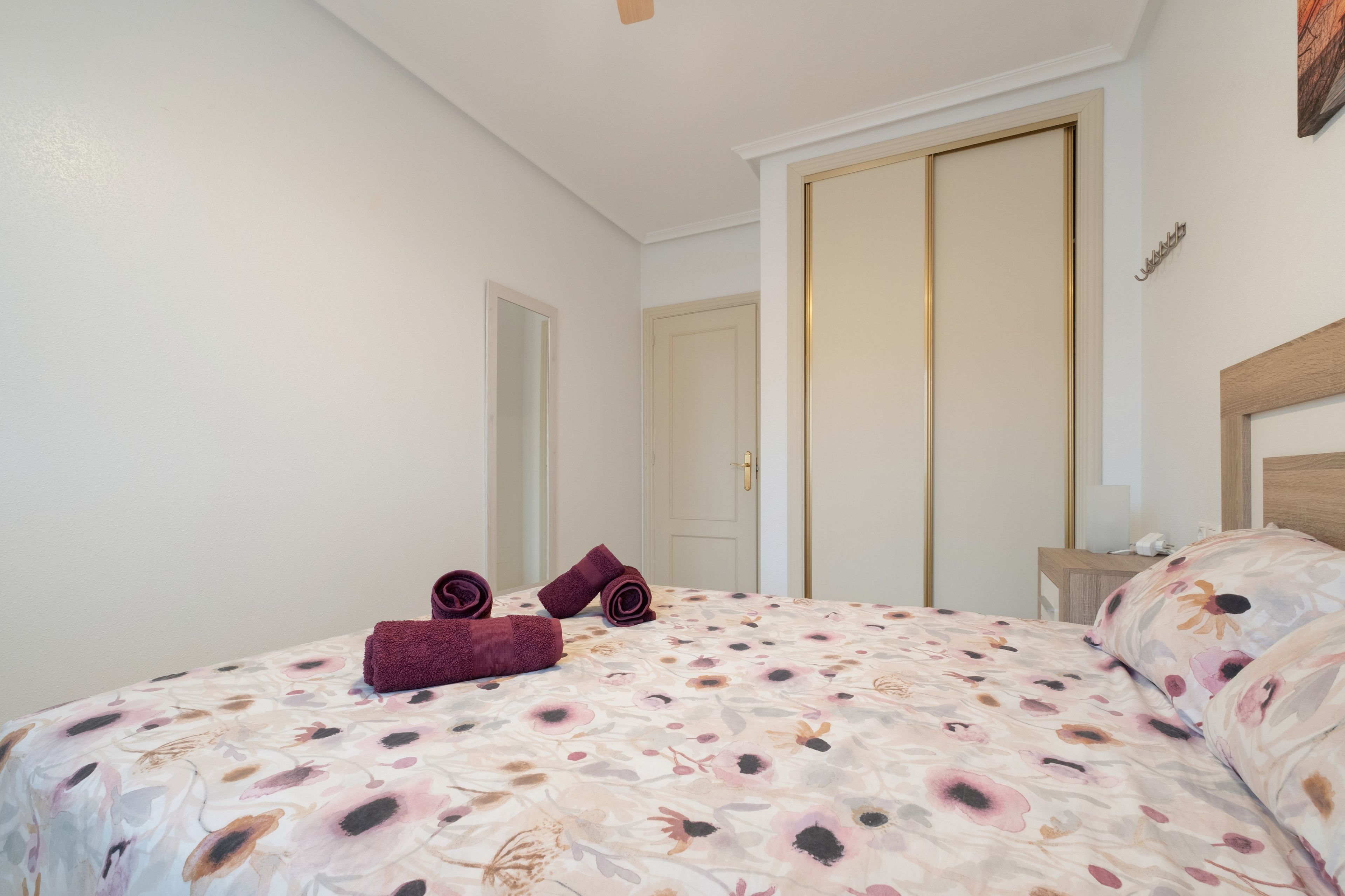 A bedroom with a bed, a nightstand, a mirror, and a door.