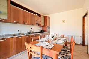 Une cuisine avec des meubles de rangement en bois, une table à manger dressée avec des assiettes et des verres, et une horloge au mur.