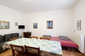 Une pièce comprenant une table à manger, deux chaises, un canapé, un lit avec une couverture colorée et trois tableaux encadrés accrochés au mur.