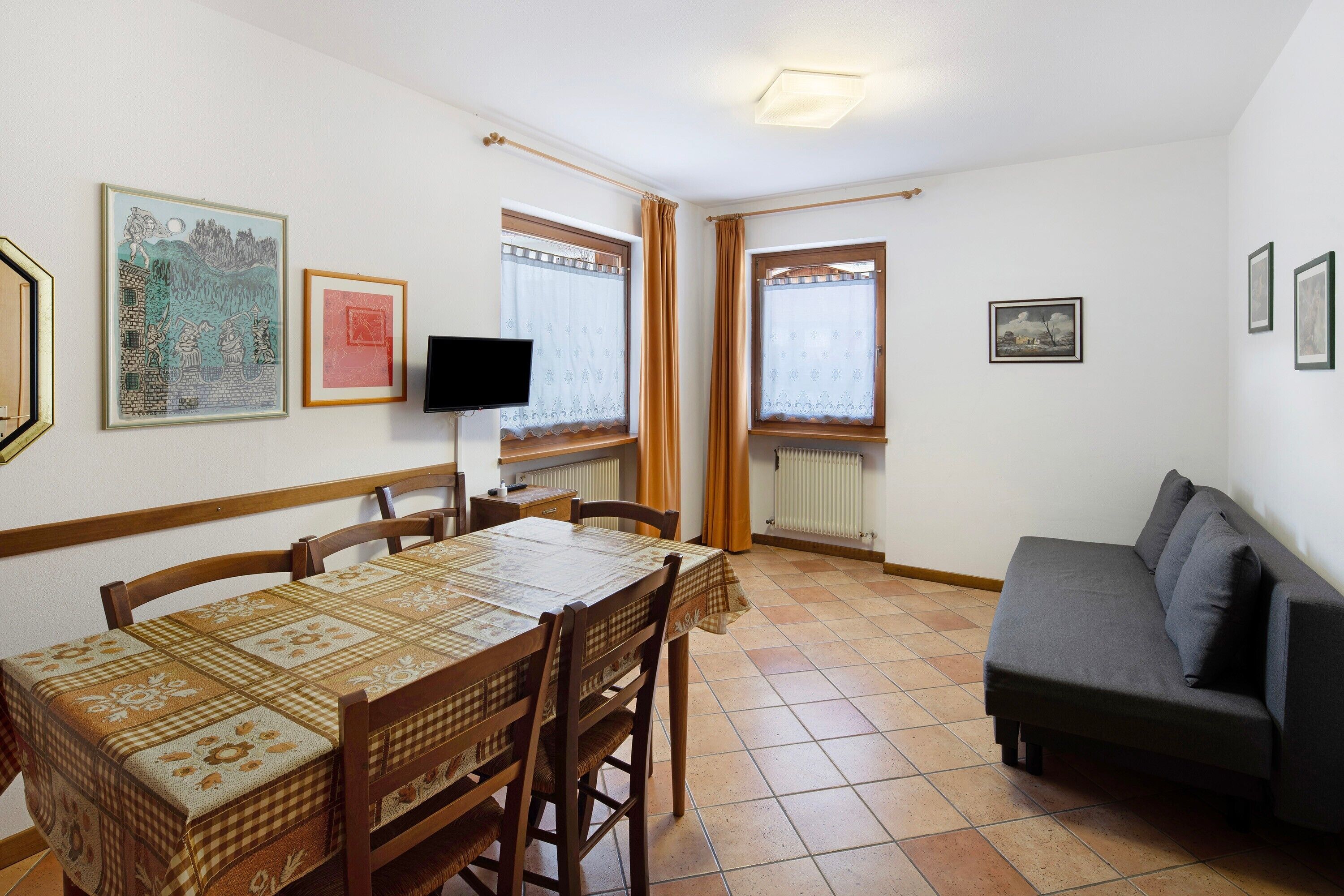 Zona pranzo con tavolo e sedie, un divano grigio e opere d'arte alle pareti.