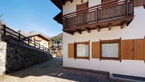 A building with a stone wall, wooden balcony, and a paved courtyard. - Apartment 'Residence Malibu Appartamento 9' with Mountain View and Wi-Fi (Falcade)