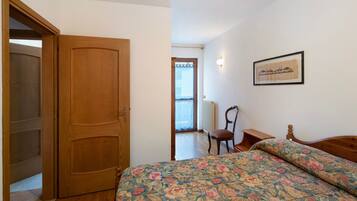 Una camera da letto con una porta in legno, un letto con biancheria da letto floreale, una sedia e un quadro appeso al muro.