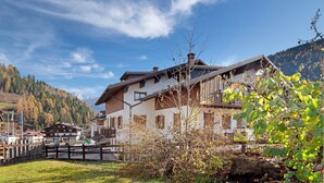 A traditional chalet-style building with a wooden facade, a sloped roof, and a mountain backdrop. - Apartment 'Residence Malibu Appartamento 9' with Mountain View and Wi-Fi (Falcade)