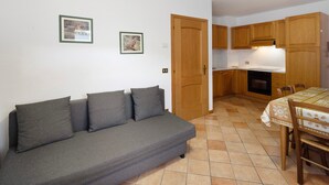 A compact living space with a sofa, a dining table, wooden cabinets, and a tiled floor. - Apartment 'Residence Malibu Appartamento 9' with Mountain View and Wi-Fi (Falcade)