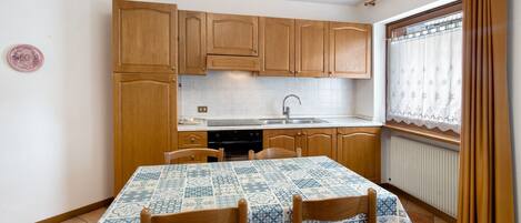 A kitchen with wooden cabinets, a tiled backsplash, a dining table with chairs, and a window with curtains.