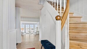 A spacious hallway with white paneled walls, a wooden staircase, and a red rug leading to a seating area with a blue bench. - Lovely home in Hjørring with sauna (Hjørring)